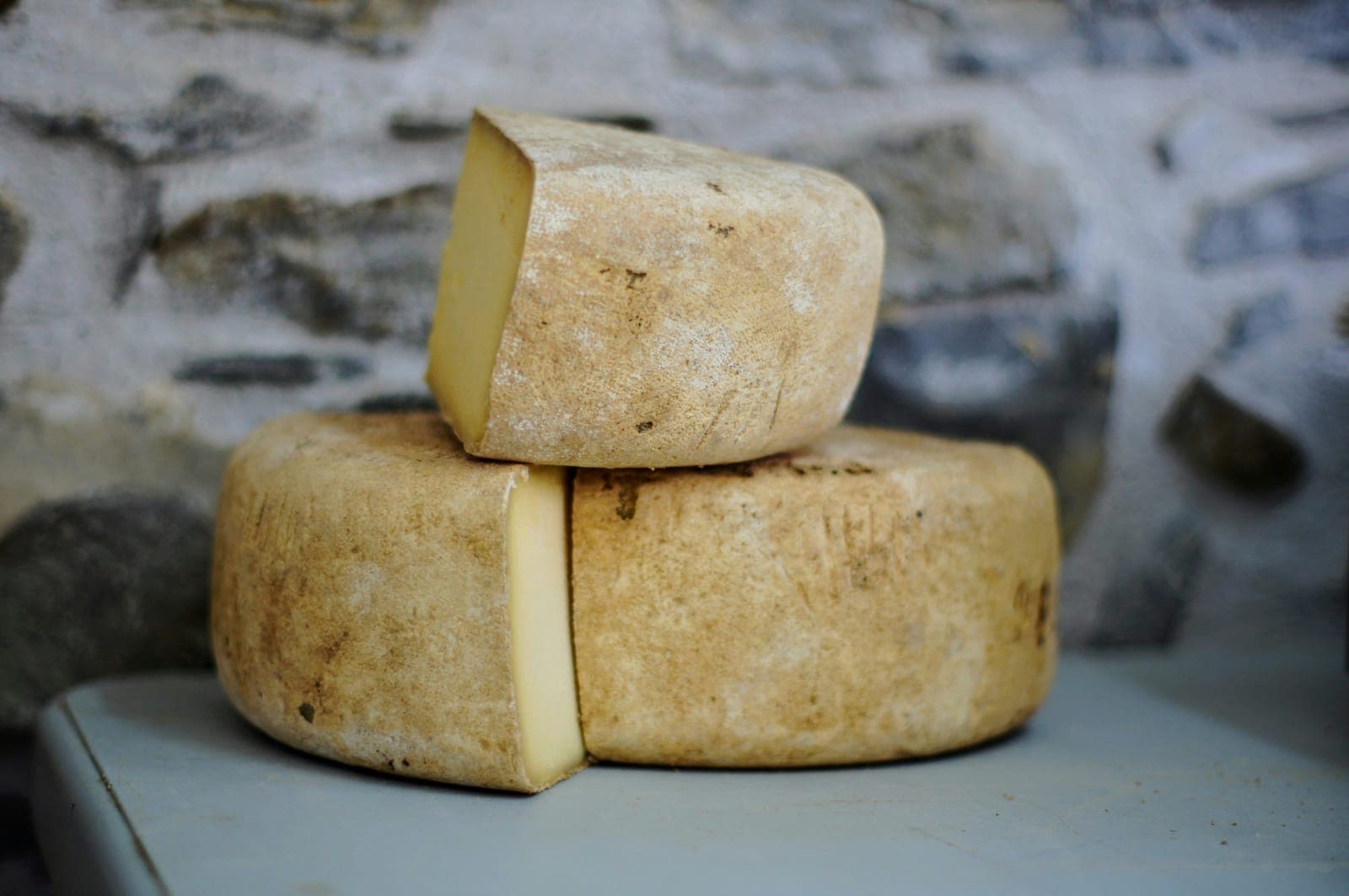 Due forme di formaggio stagionato tagliate, su una mensola davanti a un muro di pietra