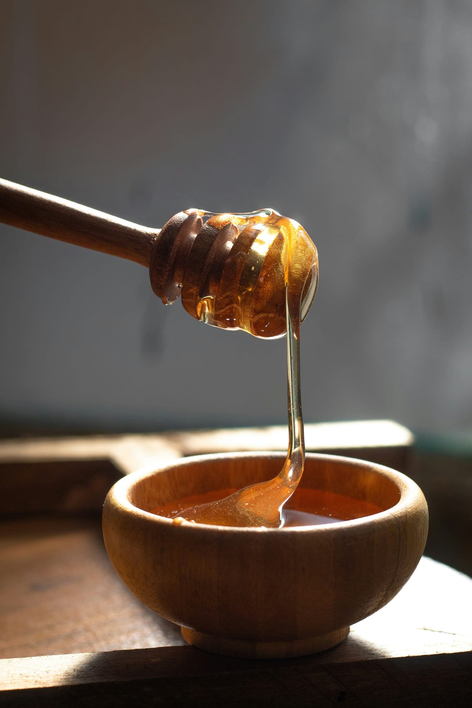 Il miele cola da un mestolino di legno in una ciotola